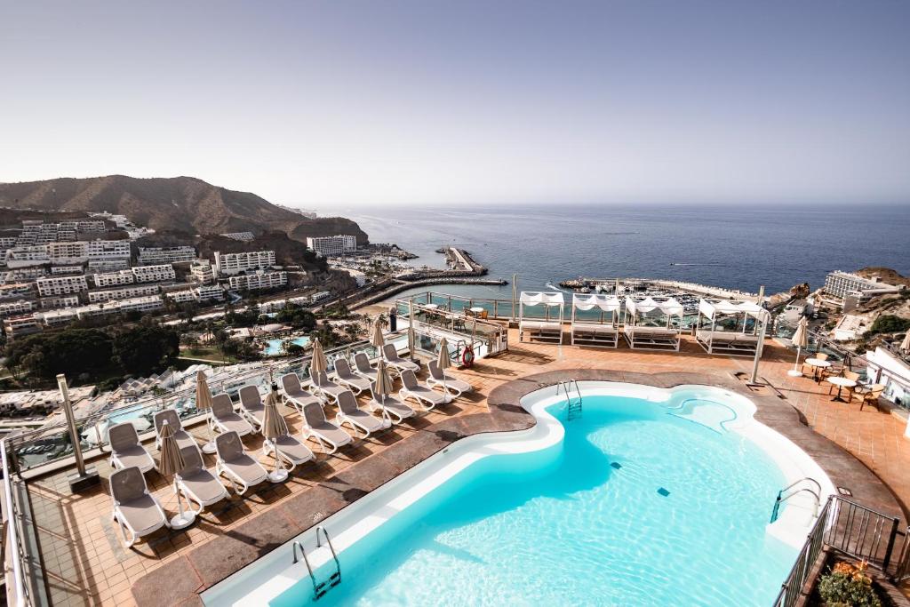 a view of a swimming pool with chairs and the ocean at Servatur JB - Adults Only in Puerto Rico de Gran Canaria