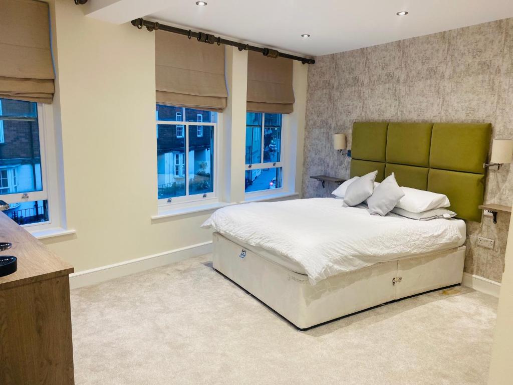 a bedroom with a bed with a green headboard and windows at The Shire Residence in Shrewsbury