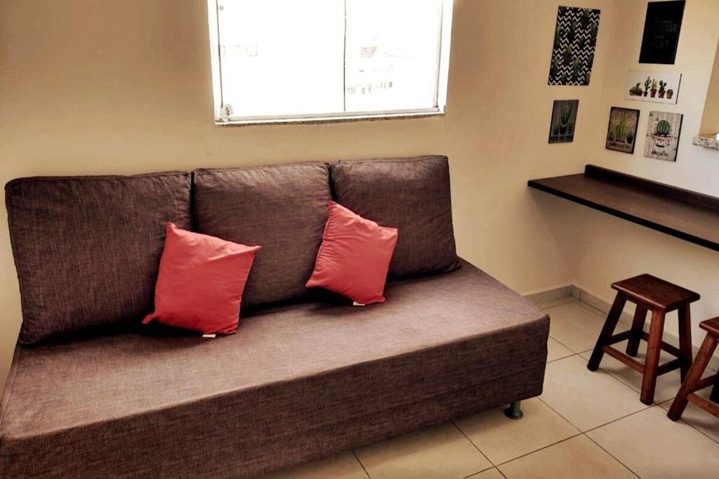 Un sofá marrón con dos almohadas rojas. en Aptos Moderno e Pratico próximo ao Teatro Paulo Moura, en São José do Rio Preto