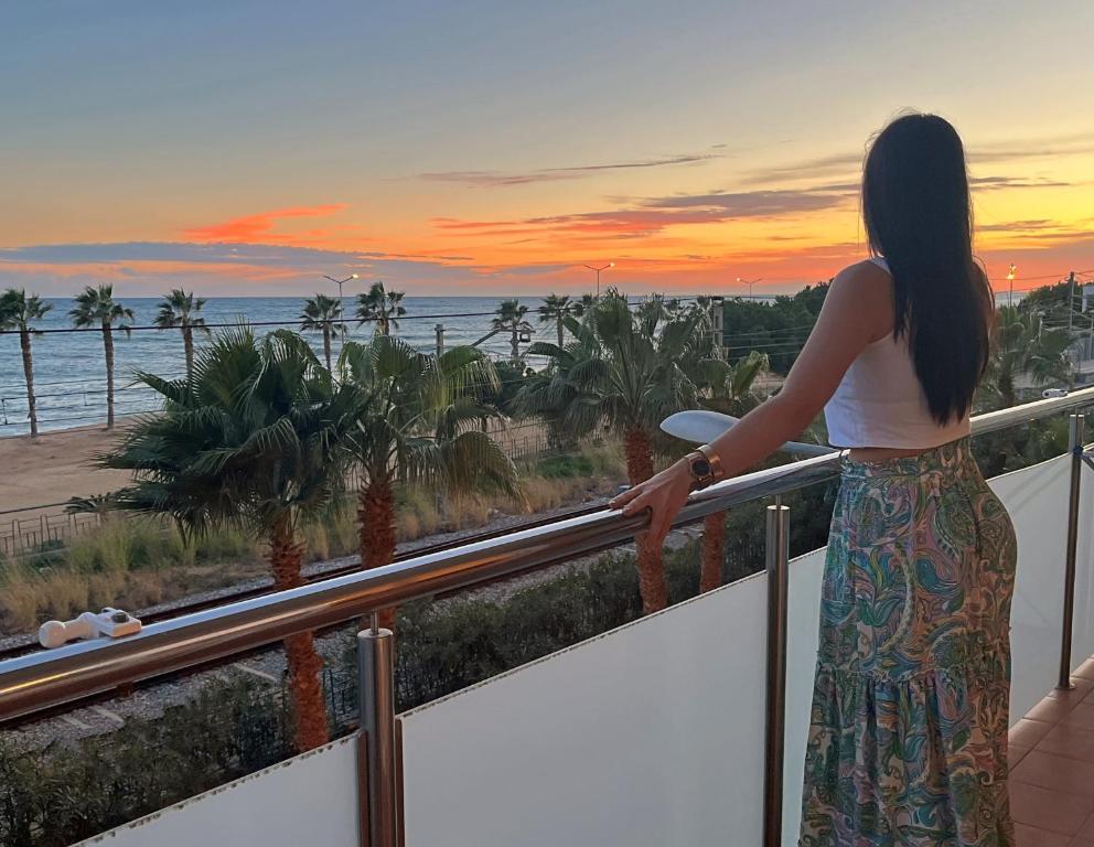 a woman standing on a balcony watching the sunset at Apartamento con vistas al mar y piscina in Pineda de Mar