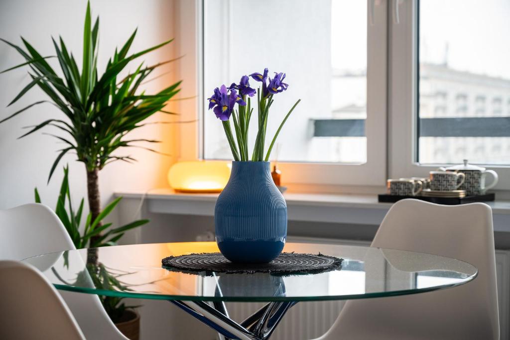a blue vase sitting on a glass table with purple flowers at Bella Luna Luxury Suites - Oasis Gem Near Stadium & Old Town in Warsaw