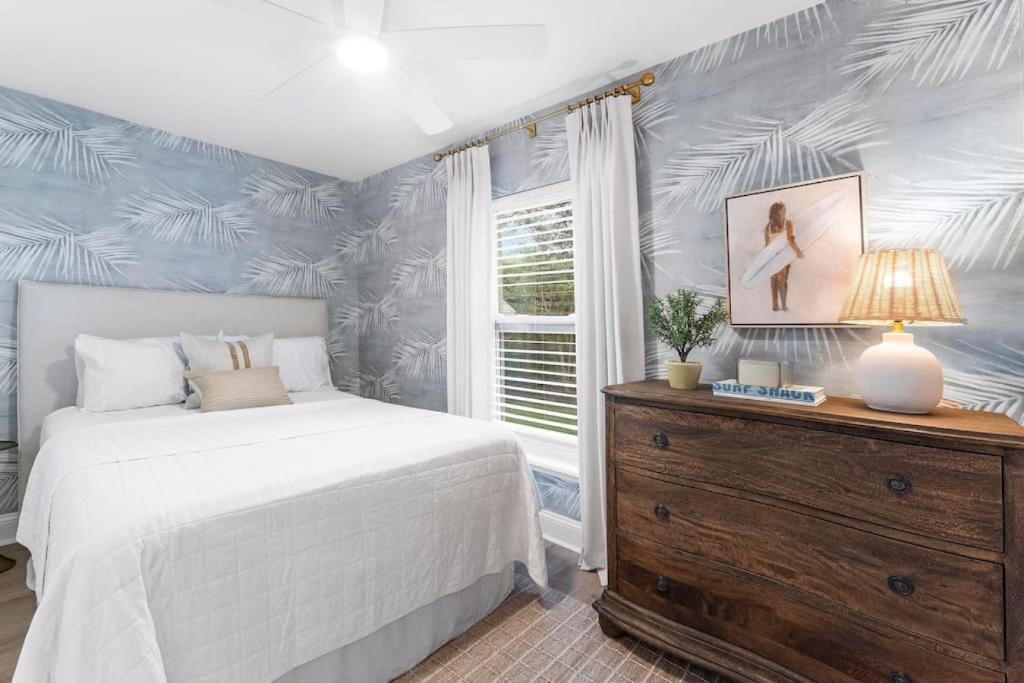 a bedroom with a bed and a dresser with a lamp at SOBE Retreat - Designers Dream - Fenced backyard in Jacksonville Beach