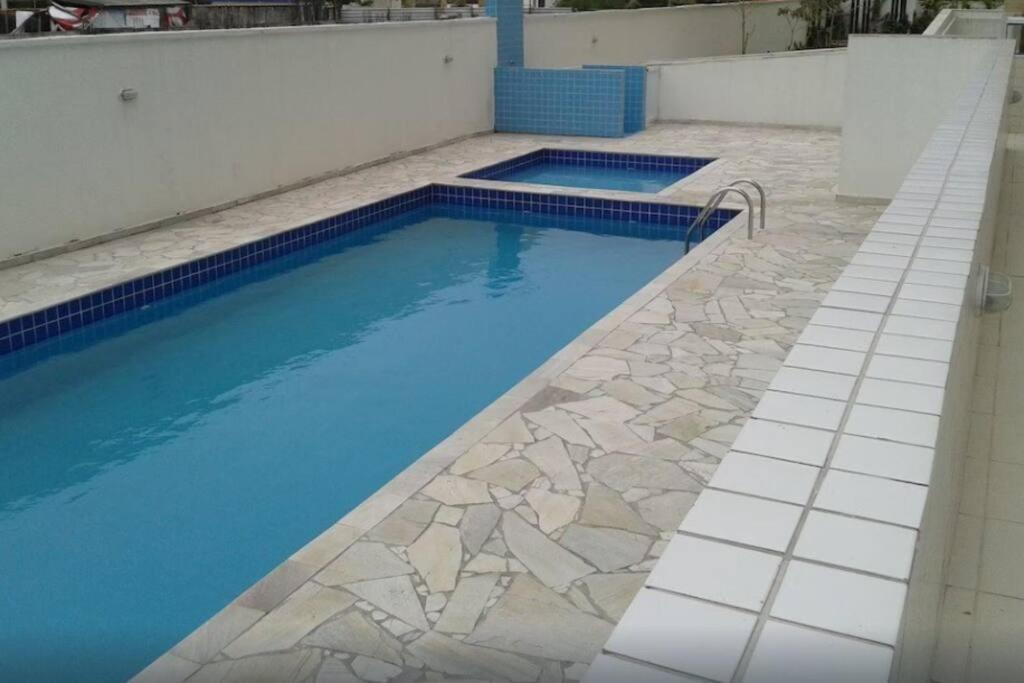 a swimming pool with blue water and stone floors at Lindo Apartamento em Bertioga/SESC a 300m da praia in Bertioga