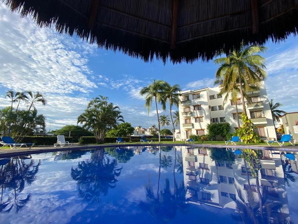 a swimming pool with palm trees and a building at Suite las palmas excelente depa con alberca in Manzanillo