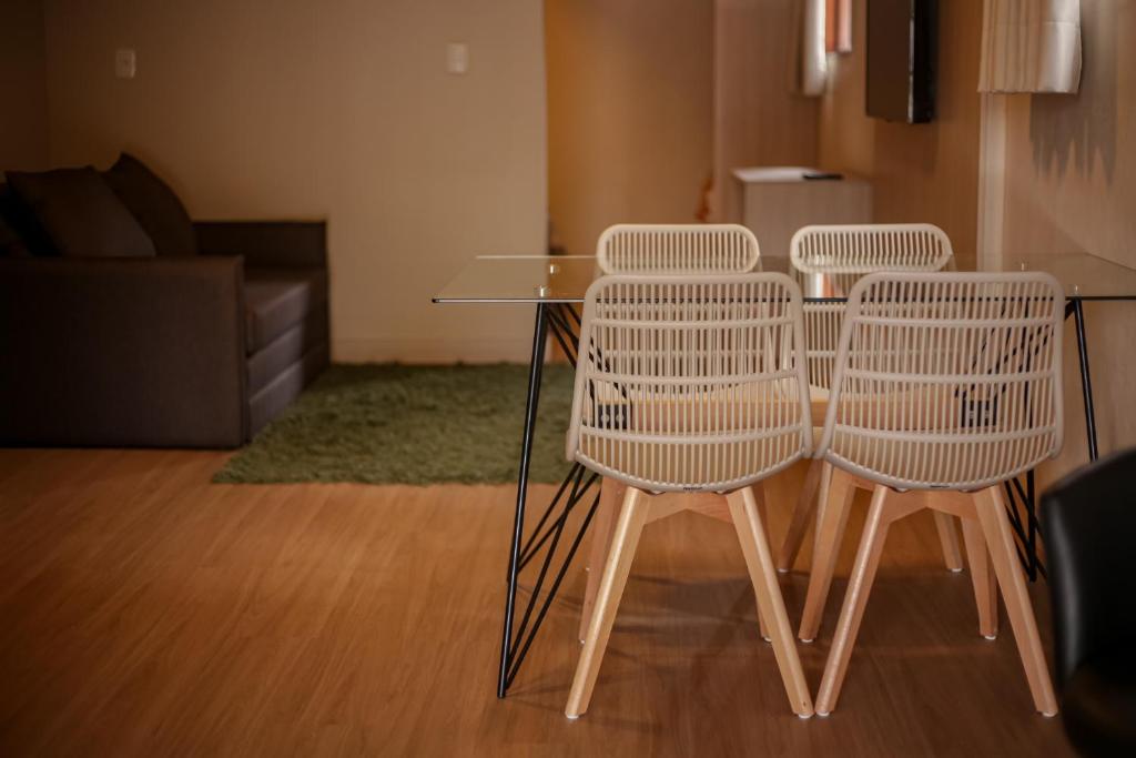 quatro cadeiras brancas à volta de uma mesa de vidro numa sala de estar em Loft completo e aconchegante em Canela