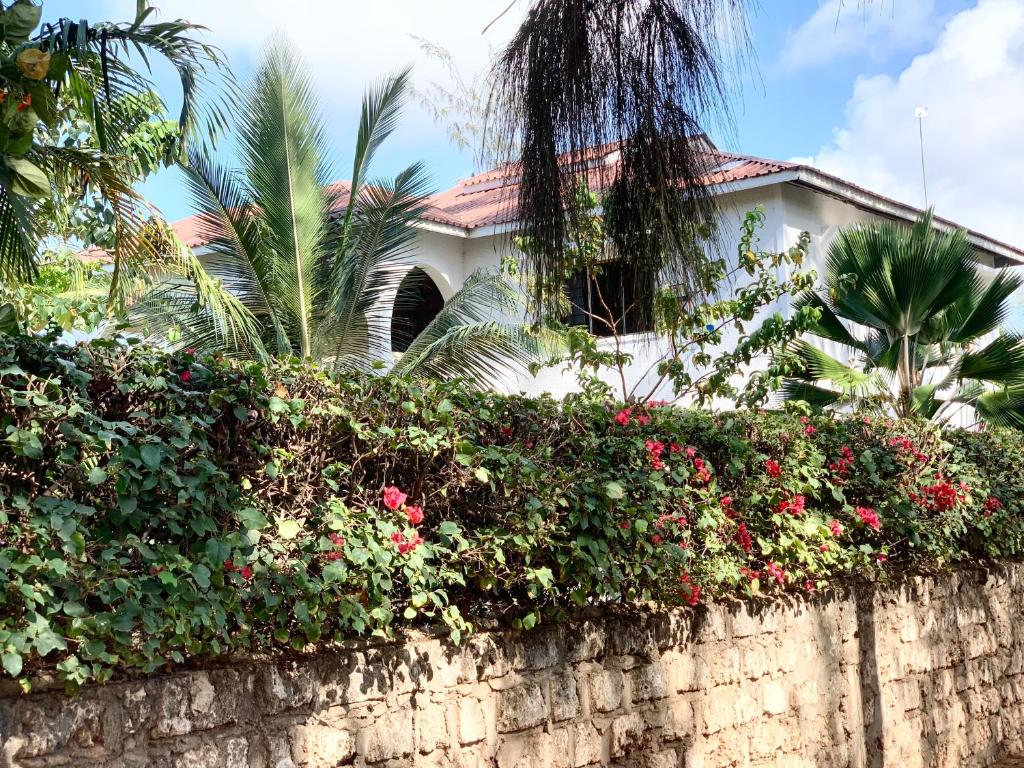 a house behind a retaining wall with flowers at Delicious House, Watamu 2-bedroom with own compound free parking and wifi in Watamu