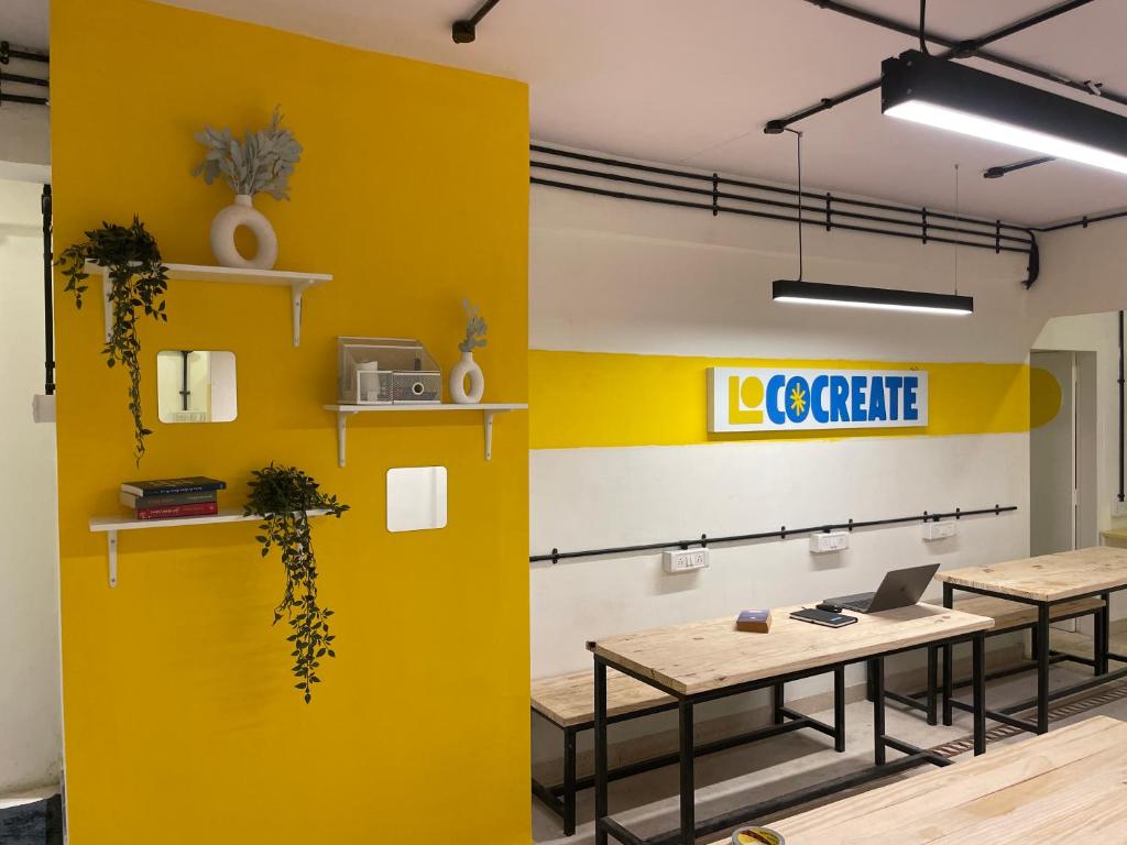 a yellow wall in an office with two tables and a laptop at Locomo Express - Stay Work Eat in Mumbai