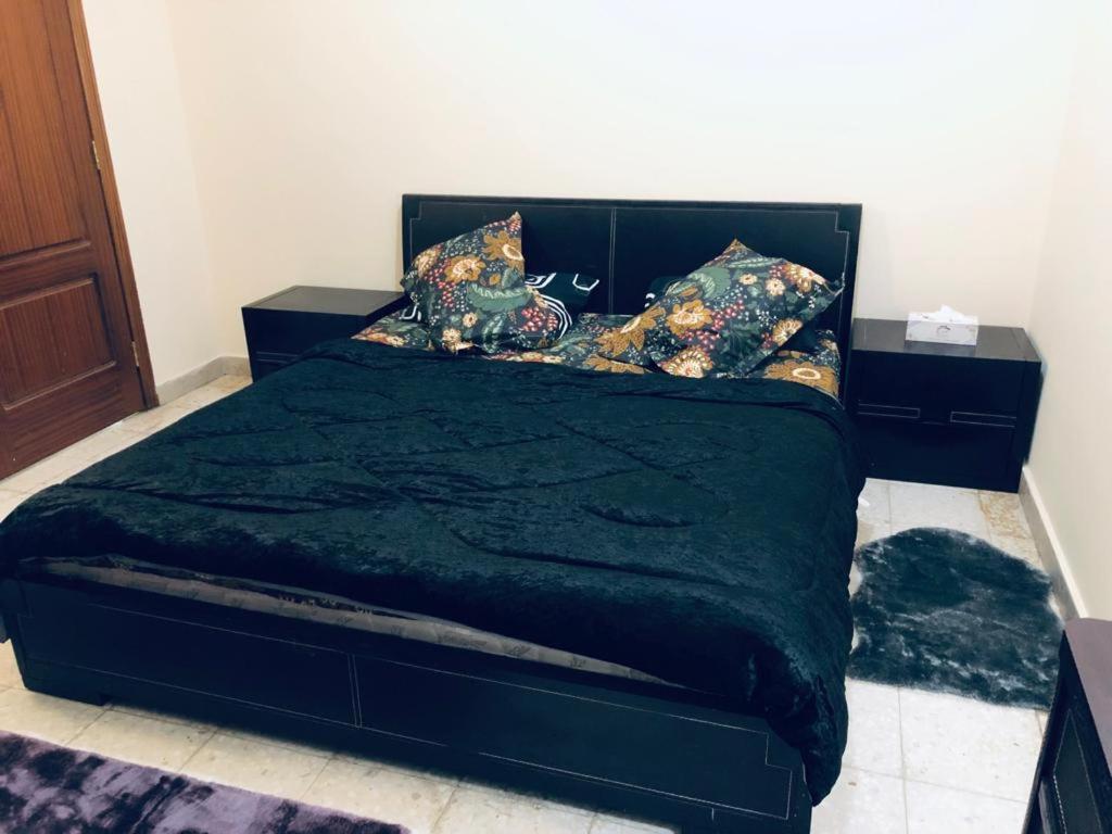 a bedroom with a bed with a black comforter and pillows at GREEN HOUSE in Al Ain
