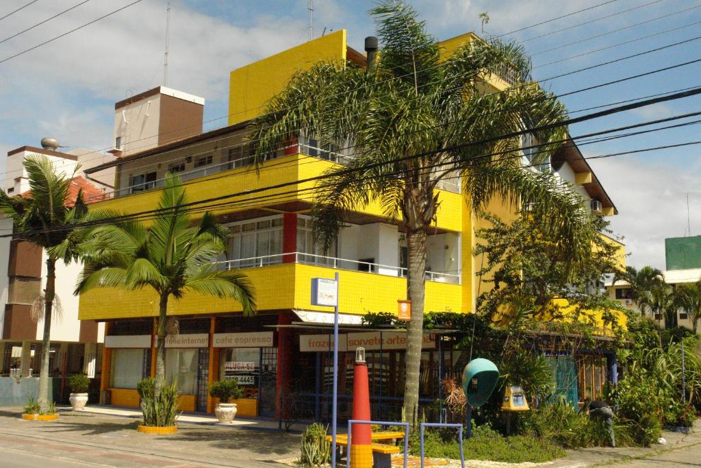 a yellow building with palm trees in front of it at Solar Diamantina Apartamentos in Florianópolis