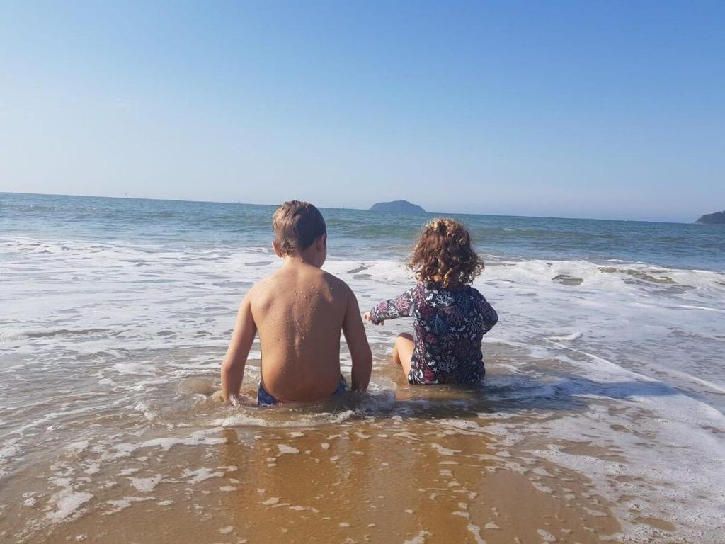 um menino e uma menina sentados na água na praia em Apartamento Aconchegante em Balneário Piçarras em Piçarras