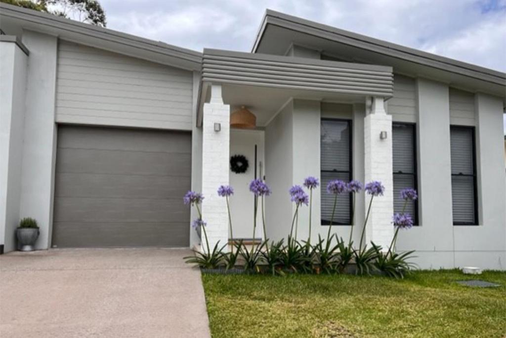 a house with purple flowers in front of it at 6A Hough Street - pet friendly, air con, wi-fi and linen provided in Nelson Bay