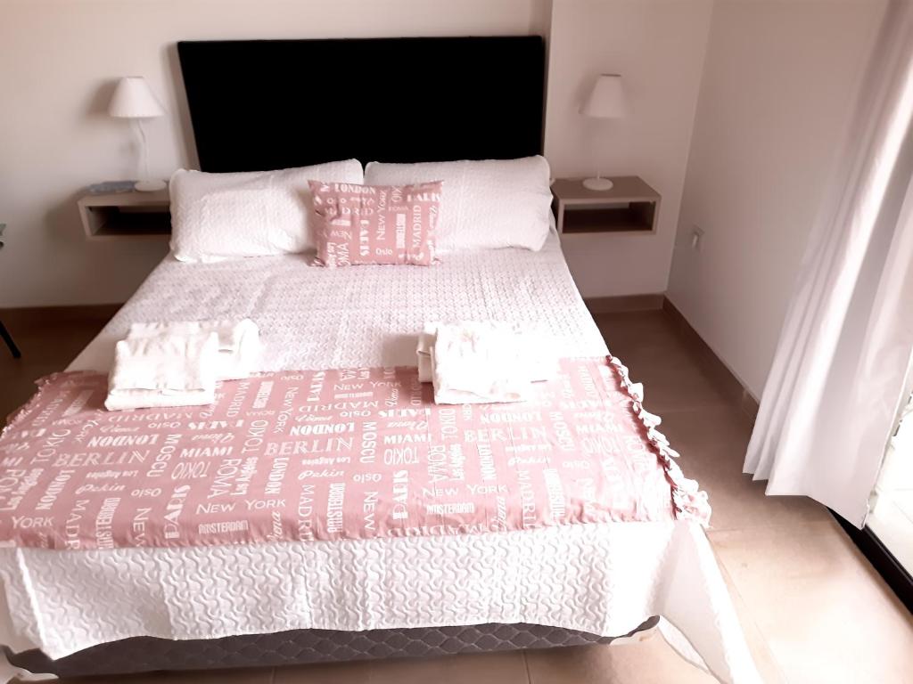 Cama grande con sábanas y almohadas rosas y blancas en Rouse en San Miguel de Tucumán
