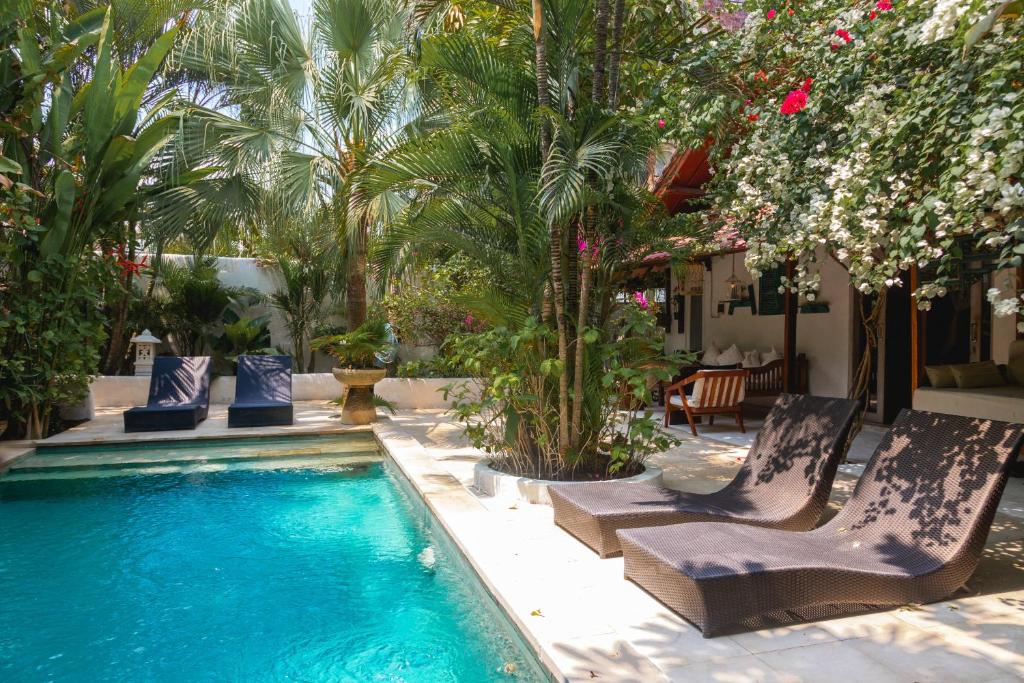 a pool with chaise lounge chairs and palm trees at Ocean Star Villa Five near the KuDeTa Beach in Seminyak