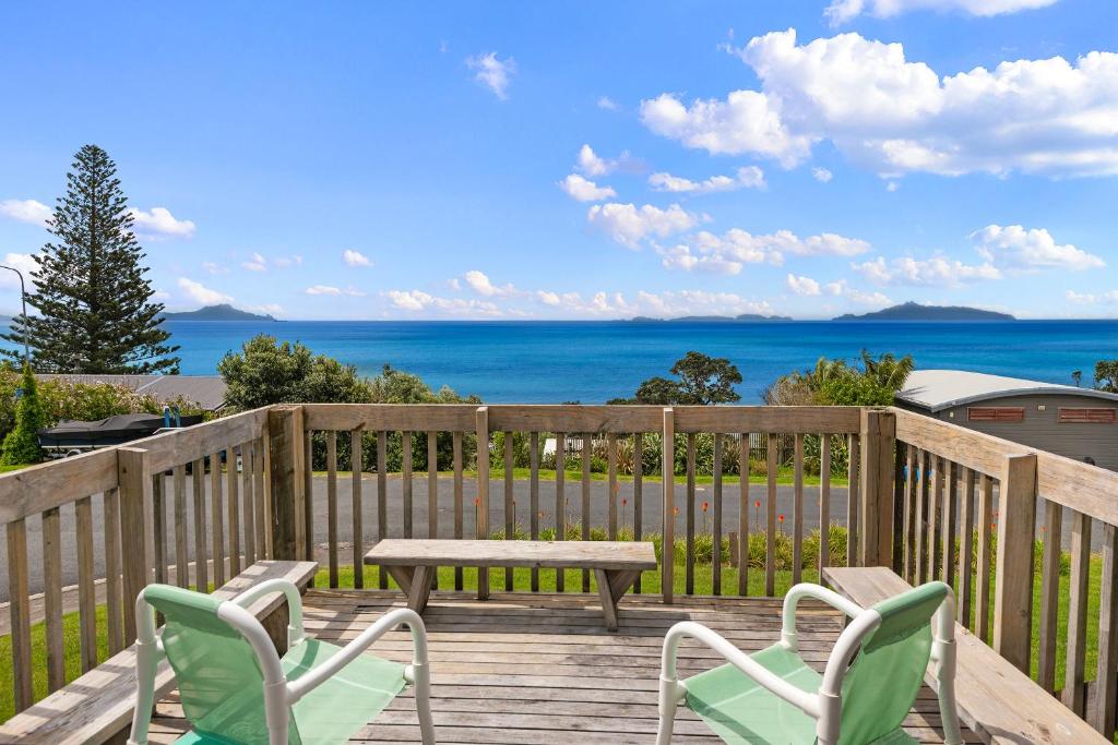une terrasse en bois avec des chaises, une table de pique-nique et l'océan dans l'établissement Bay View Bach - Langs Beach Holiday Home, à Waipu