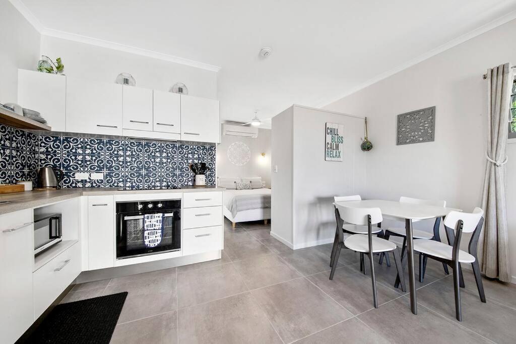 a kitchen with white cabinets and a table and chairs at Modern Luxury Studio Apartment in Emu Park