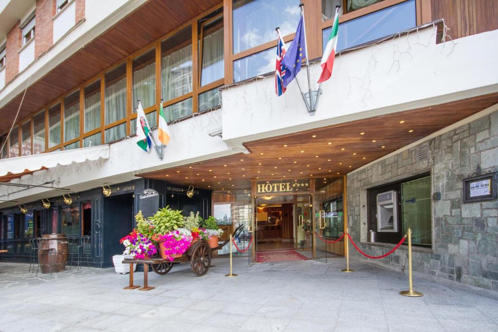 un bâtiment avec une charrette avec des fleurs devant lui dans l'établissement Relais Des Alpes, à Sauze dʼOulx