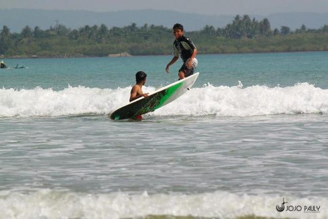 Zwei Menschen reiten auf einem Surfbrett im Ozean in der Unterkunft Casa Vacanza Bungalow-Dagat-Dagatan Beach Camp in Gubat