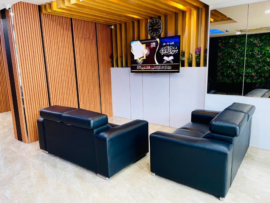 A lobby lounge with four black leather seats facing a wall-mounted television.
