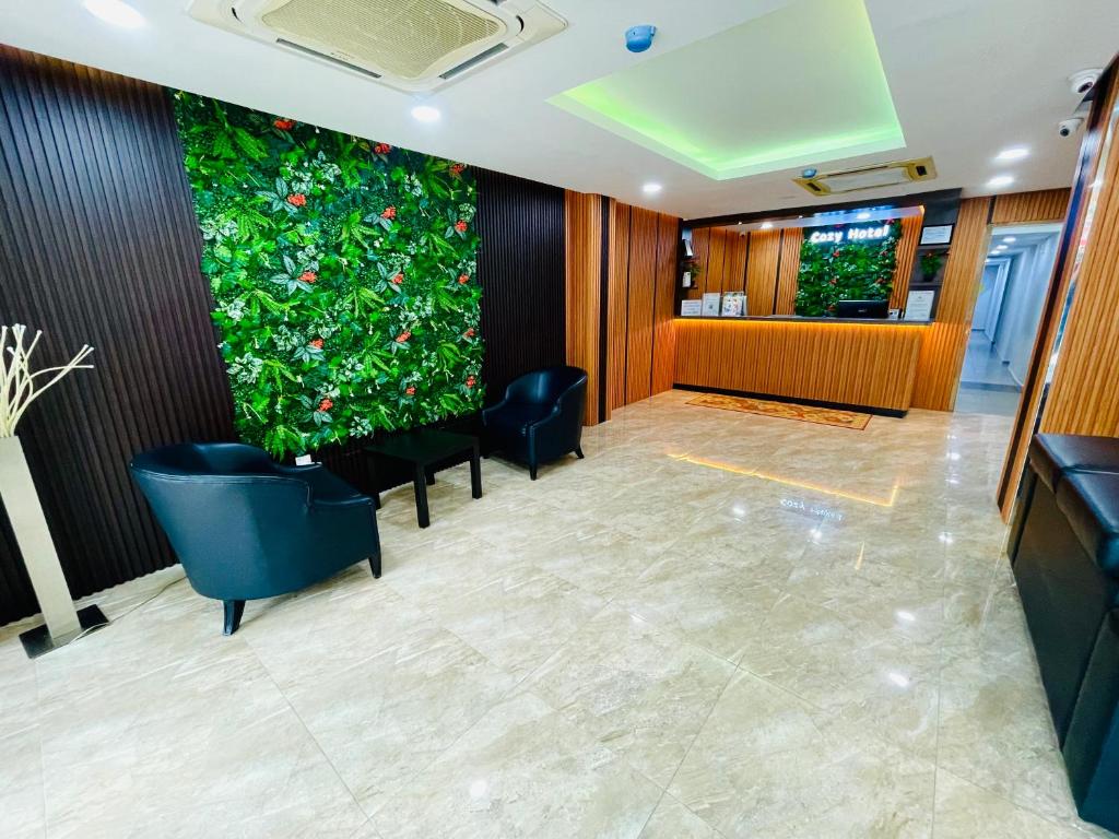 A bright lobby with black lounge chairs and a leafy feature wall.