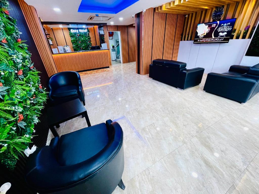 A hotel waiting area with black lounge seating, a television and reception beyond.