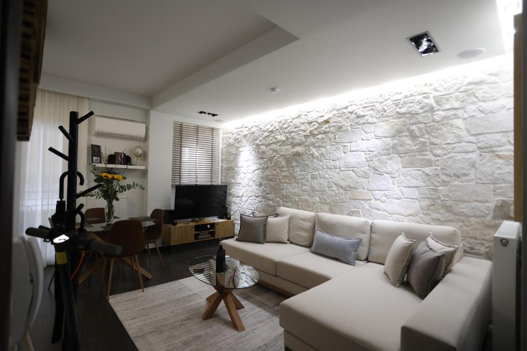 LA Larissa Luxury Apartments Thetis في لاريسا: غرفة معيشة مع أريكة بيضاء وجدار حجري
