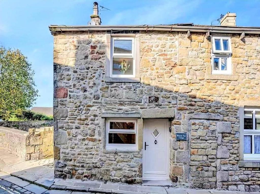 a stone house with a white door and windows at Blossom Tree Cottage in Barnoldswick