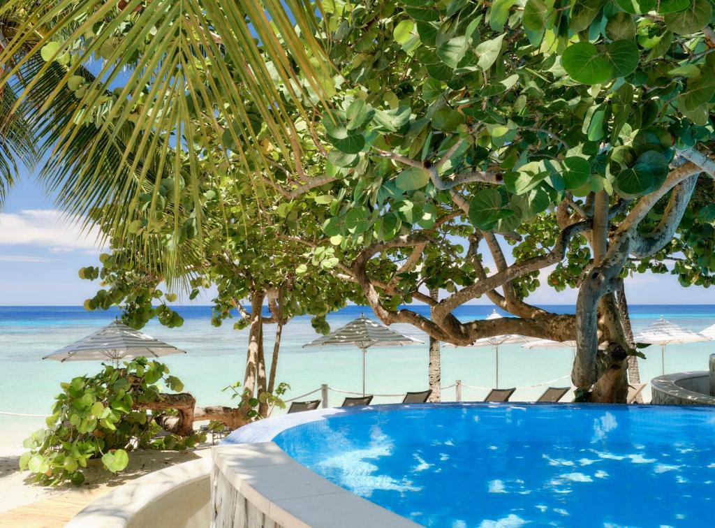 a swimming pool next to a beach with umbrellas at Kimpton - Grand Roatan Resort and Spa in West Bay