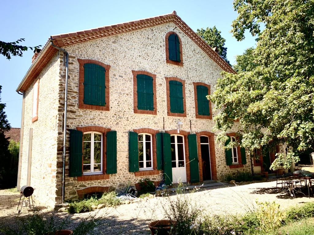 una antigua casa de piedra con ventanas con persianas verdes en Sous le Tilleul de la Condomine, grand gite piscine privee, en Payrin-Augmontel