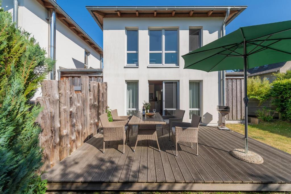 eine Holzterrasse mit einem Tisch und einem grünen Sonnenschirm in der Unterkunft Ferienhaus an der alten Gärtnerei - Rosmarin in Heiligendamm