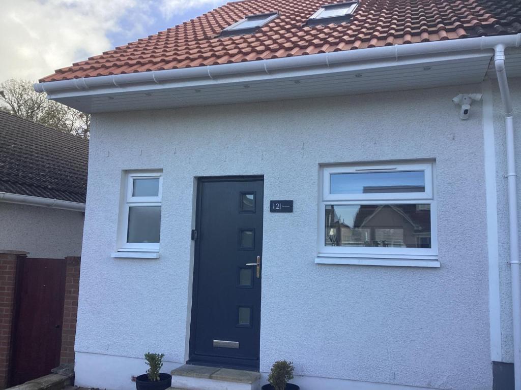 uma casa branca com uma porta preta e um telhado vermelho em The Annexe em Eaglesham