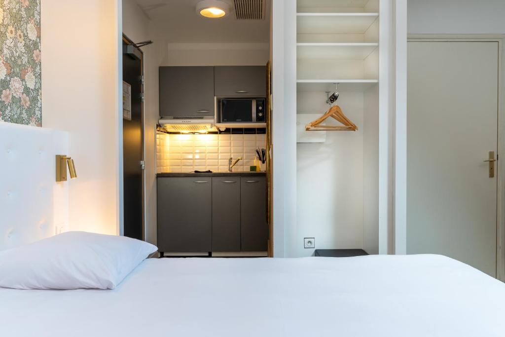 a bedroom with a white bed and a kitchen at CALM Appart' & Hostel in Lille