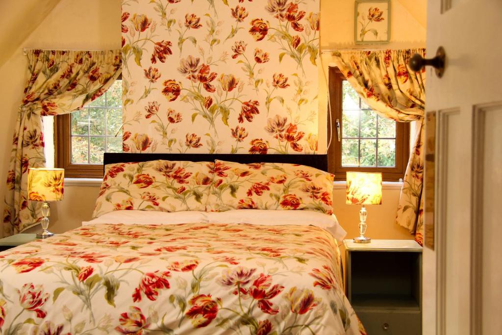サウス・モルトンにあるWest Down Farmhouseのベッドルーム1室(花柄のベッドカバー、窓2つ付)