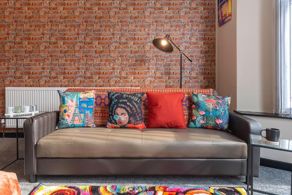 赫爾河畔京士頓的住宿－Hull 1 Bedroom Apt 3 beds Spacious Jesouth Striking，砖墙间里一张长沙发,上面有色彩缤纷的枕头