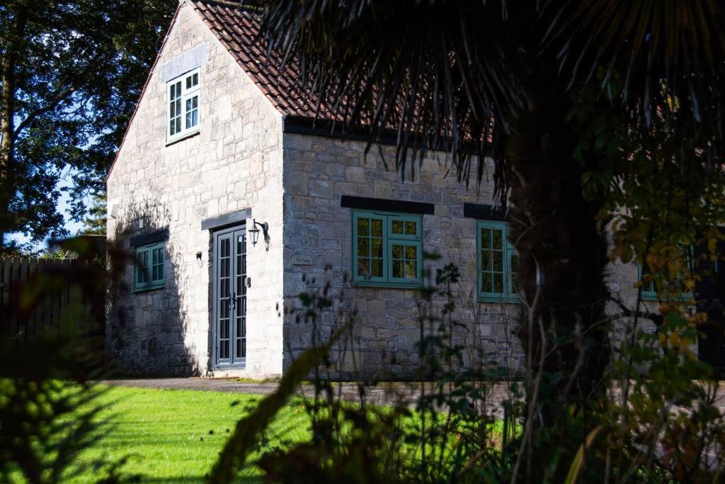 an old stone building with green windows on a field at The Snug, Beautiful Country Retreat in Priston