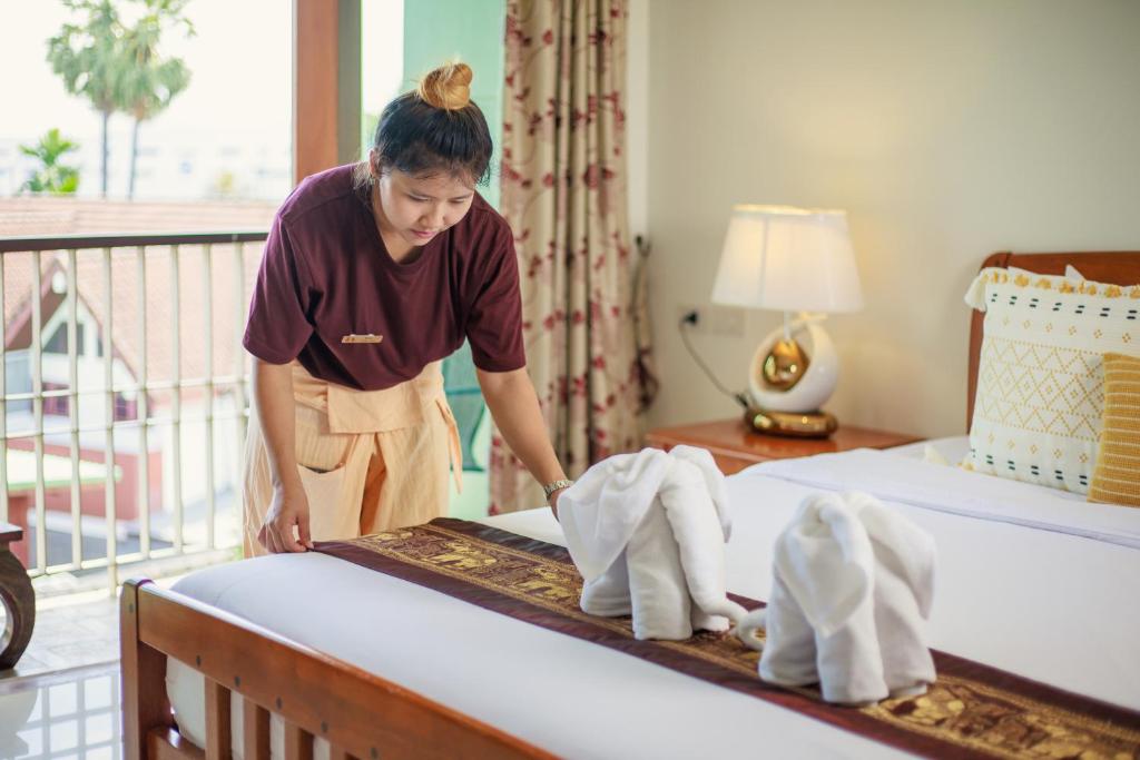 a woman putting towels on a bed in a hotel room at Rendezvous Classic House in Chiang Mai