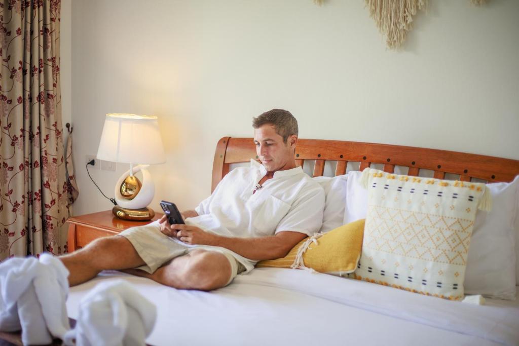 a man sitting in a bed holding a cell phone at Rendezvous Classic House in Chiang Mai