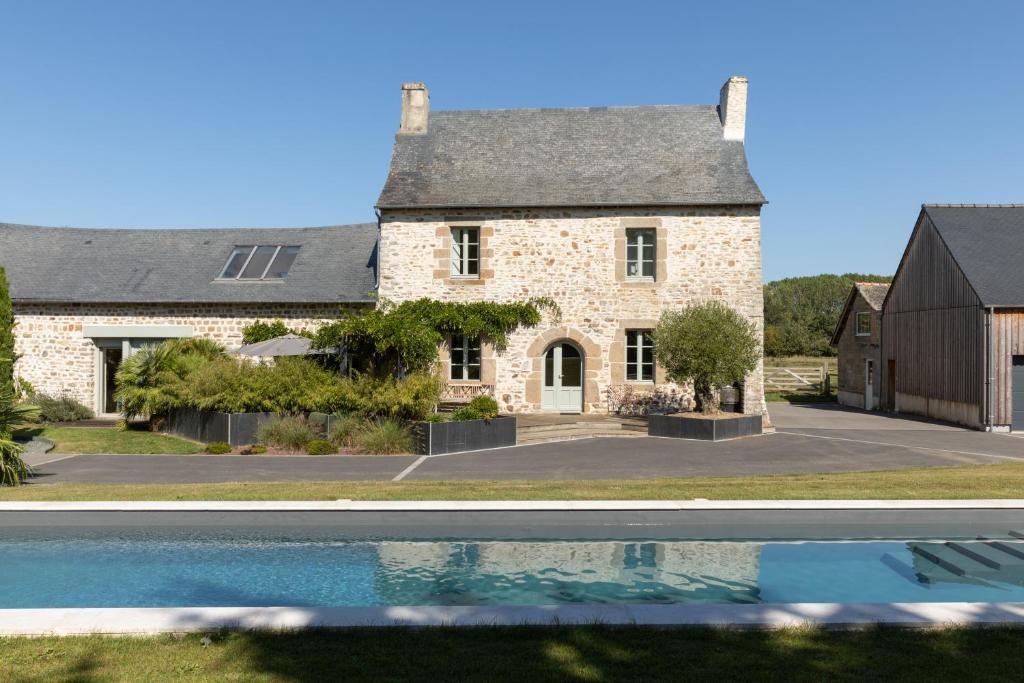una casa de piedra con piscina frente a ella en Maison cosy avec Spa privatif et piscine chauffée près Vitré et Rennes, en Val-dʼIzé