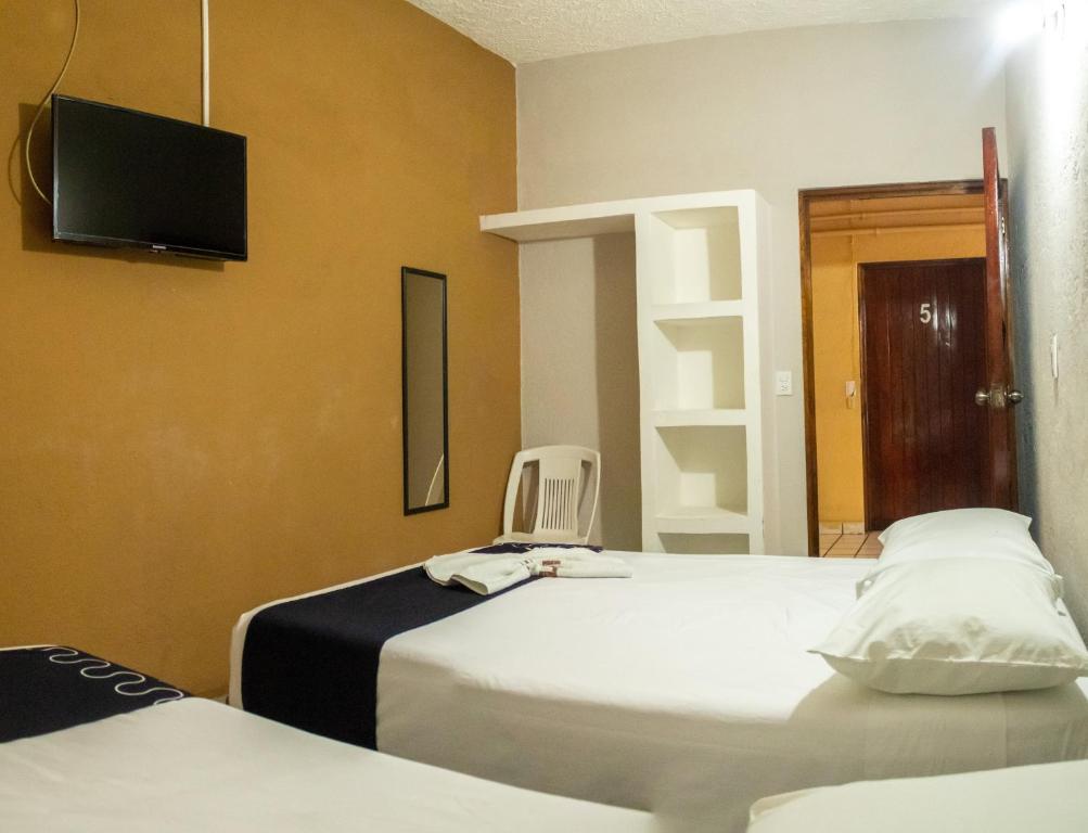 a room with two beds and a chair and a tv at Hotel Colonial in Zihuatanejo