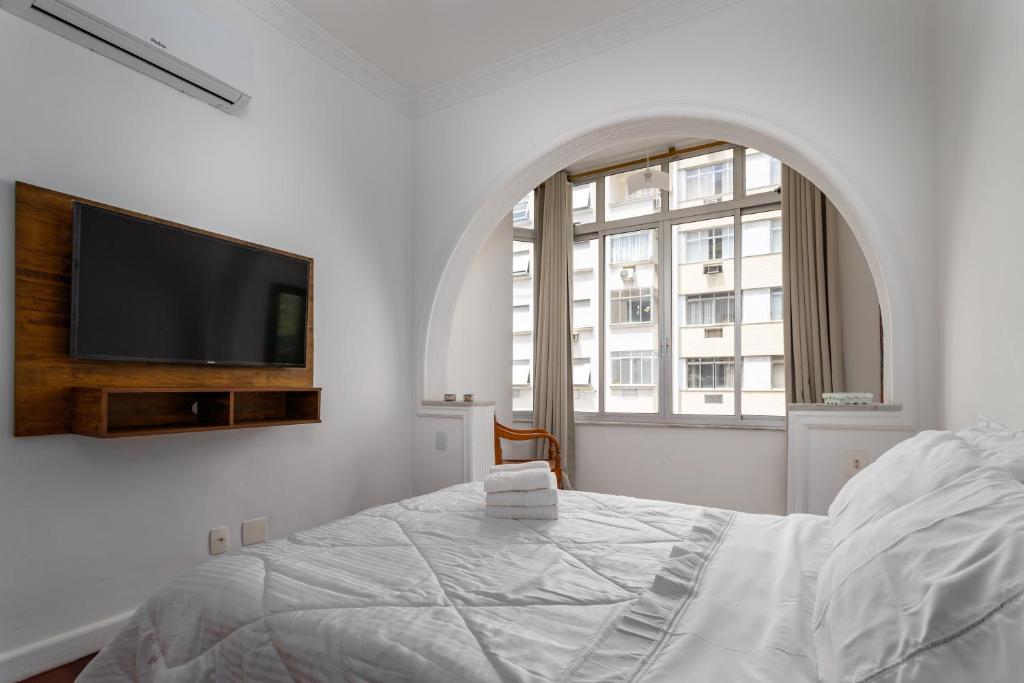 a white bedroom with a bed and a flat screen tv at Apartamento aconchegante em Copacabana - Rio de Janeiro in Rio de Janeiro