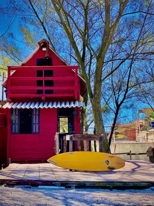 a yellow surfboard sitting in front of a red house at Chalé Aloha Ihul ! O paraíso pé na areia ! in Arraial do Cabo