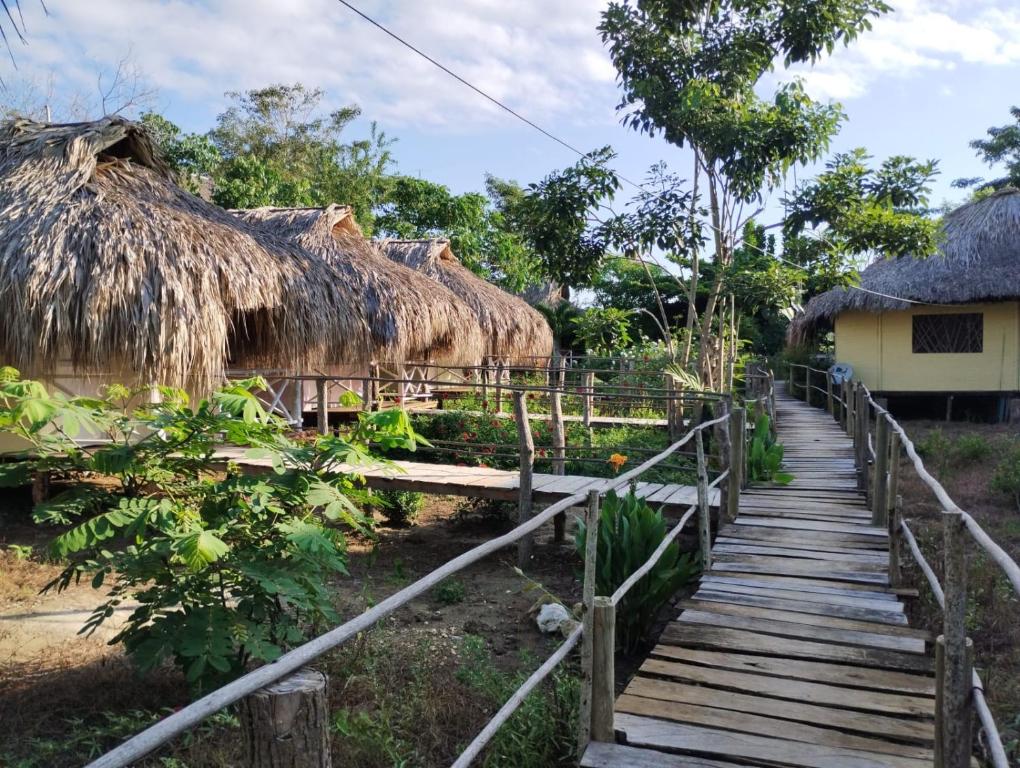 um caminho de madeira que leva a uma aldeia com cabanas de palha em Cabañas La Múcura em San Onofre