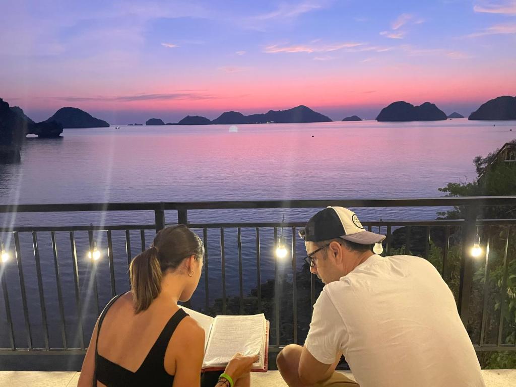 a man and woman sitting on a balcony looking at the ocean at LePont Cat Ba Bungalow in Cat Ba