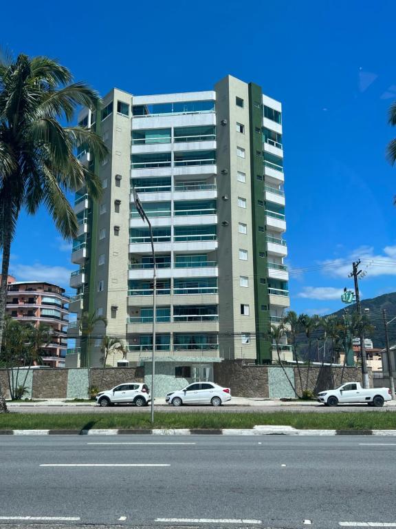 a tall building with cars parked in front of it at Apto beira mar pé na areia in Caraguatatuba