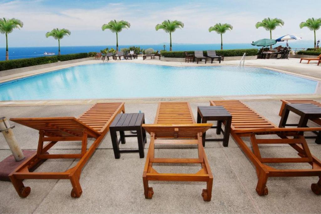 a swimming pool with wooden tables and chairs next to it at Markland Seaside Pattaya in Pattaya Central