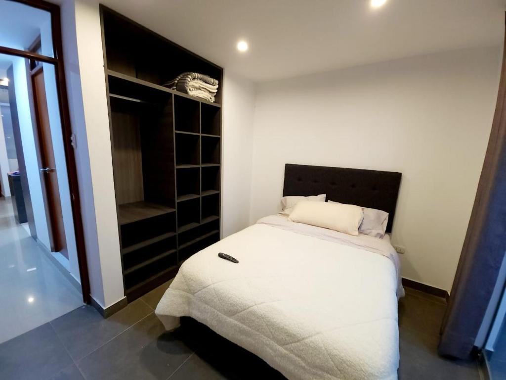 a bedroom with a white bed and a closet at Acogedor departamento en Huacachina in Ica