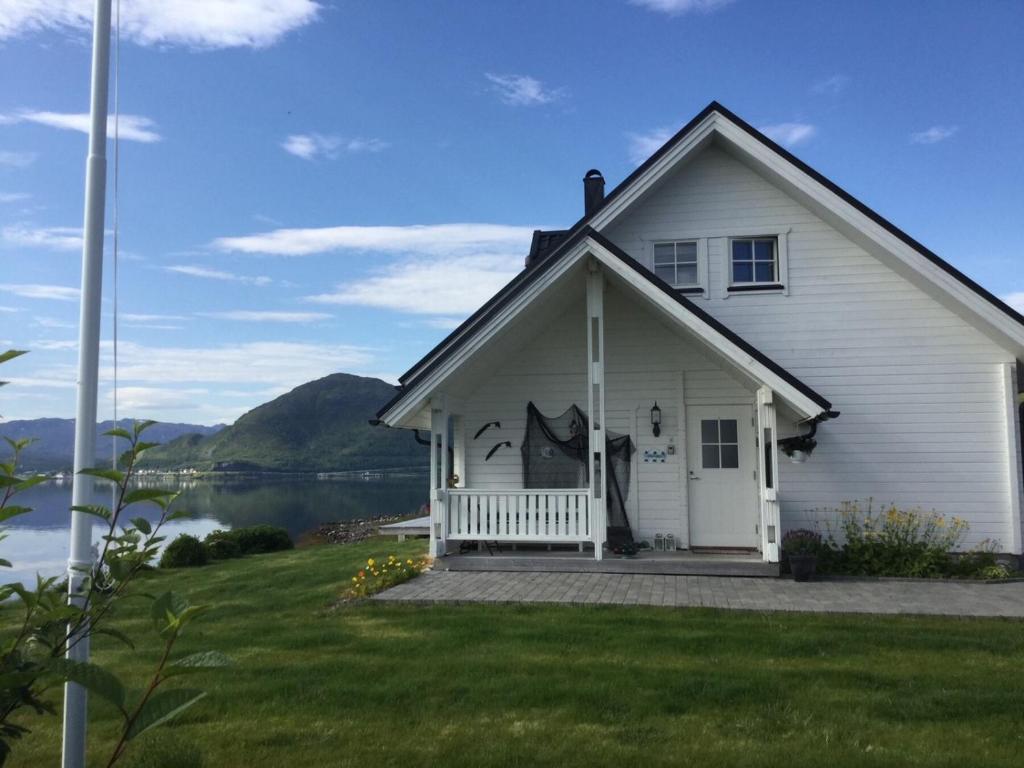 une maison blanche avec une terrasse couverte à côté d'une étendue d'eau dans l'établissement Idyllisk hus ved sjøen, à Hammerfest