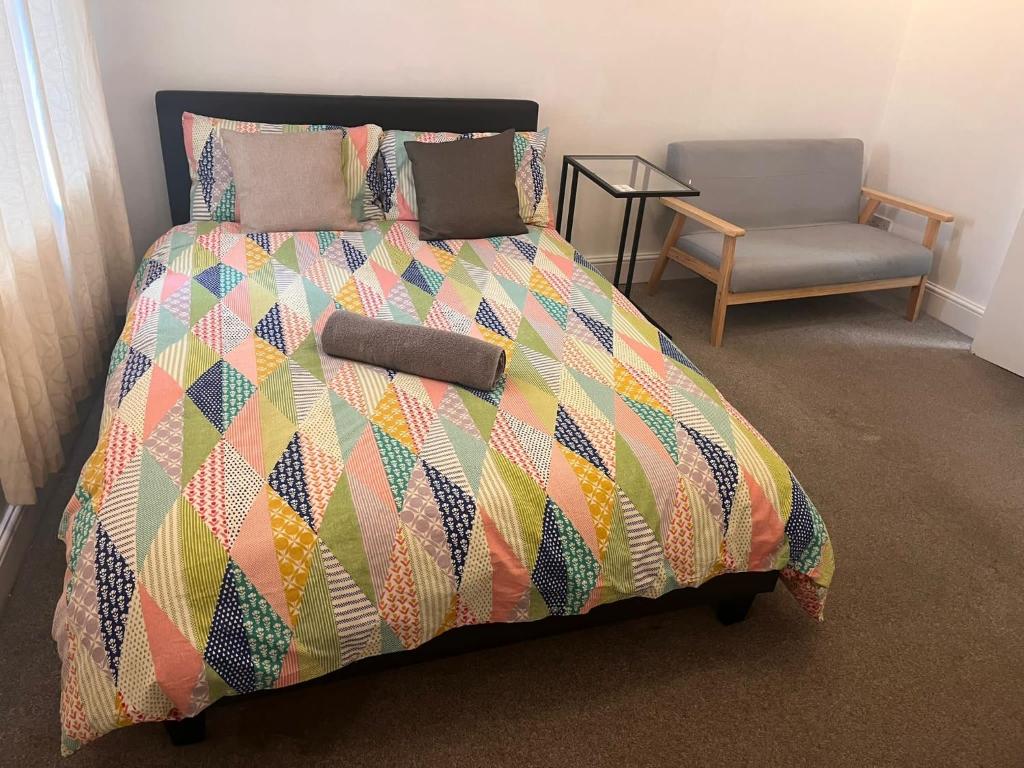 a bed with a colorful comforter and a chair at SouthStreet Suites in Isleworth
