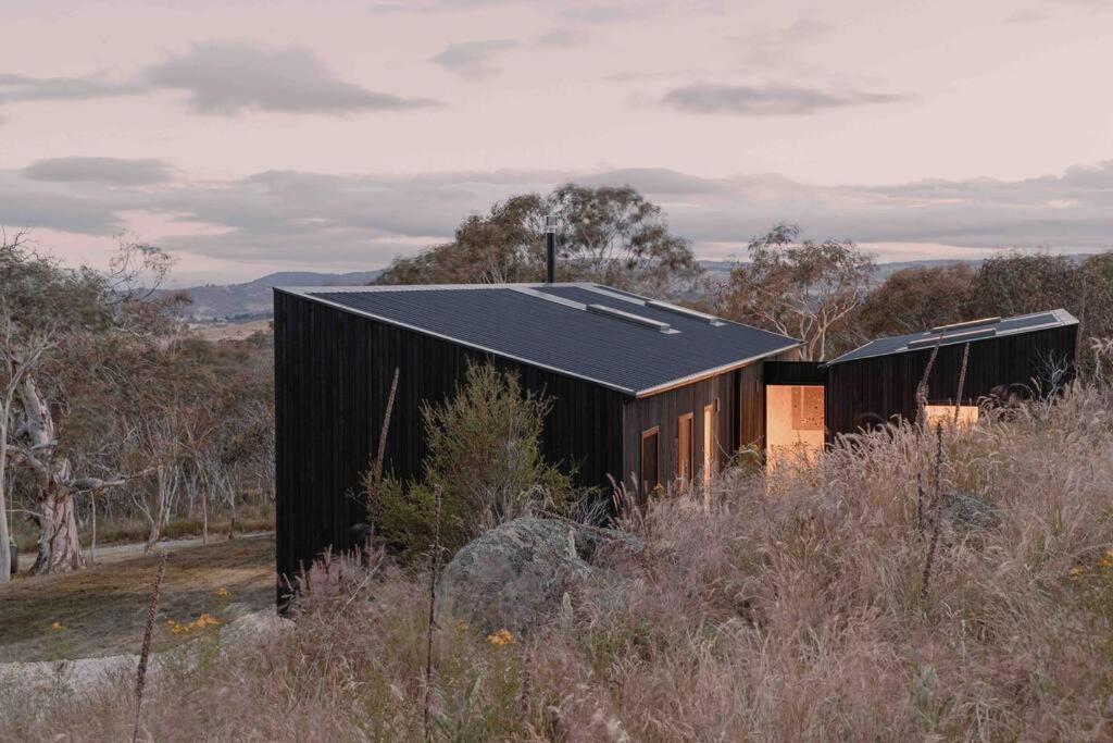 a black house in the middle of a field at Common Kosci - luxury bespoke cabin in the Snowies in Jindabyne