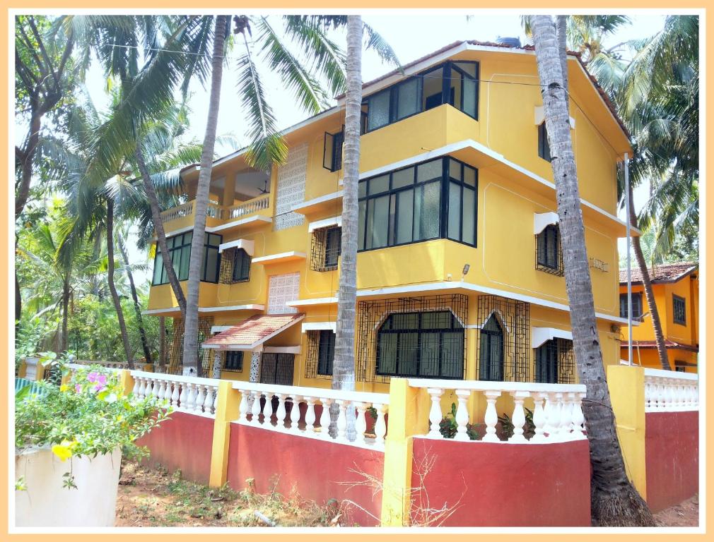 a yellow building with palm trees in front of it at Shalom Guest House in Candolim