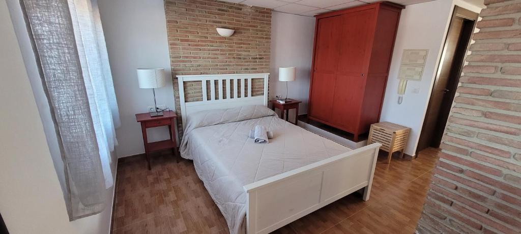 1 dormitorio con 1 cama blanca con 2 mesas y pared de ladrillo en Apartamentos luna, en Ardales